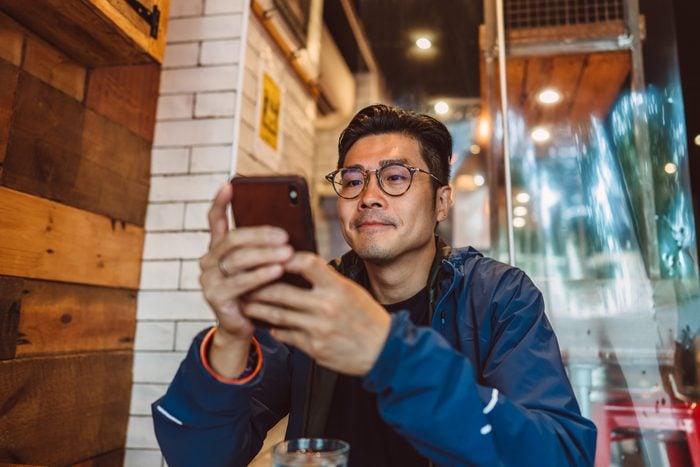 Young handsome Asian man making order from the digital menu on smartphone in restaurant