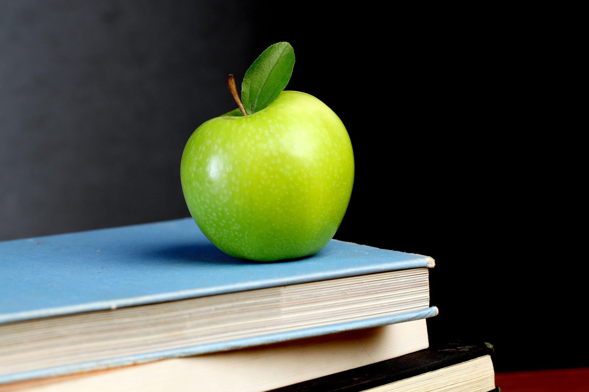 Granny smith apple on stack of books on a teacher's desk