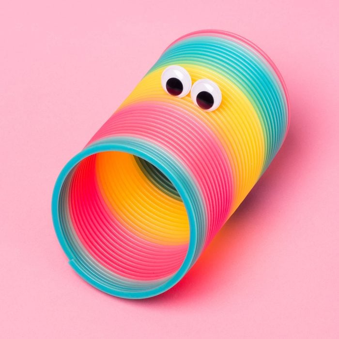 colorful slinky with googly eyes posed to resemble a funny face on pink background