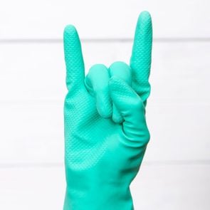 Hand In green cleaning Glove Showing Rock Sign with white tile background