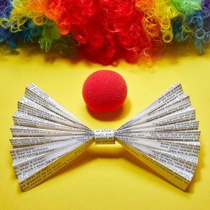 origami bowtie made from funny poetry page, red clown nose, and rainbow clown wig on yellow background