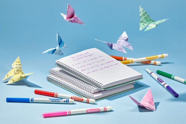 poetry written on lined notebook paper with some markers scattered around and origami butterflies made with poetry pages floating above; light blue background