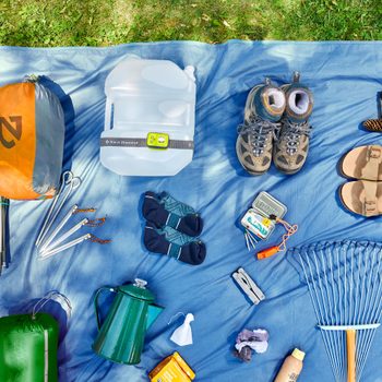 Camping supplies spread out on a tarp in the grass