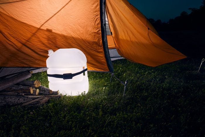 a lamp made from a plastic jug and a headlamp outside an orange tent