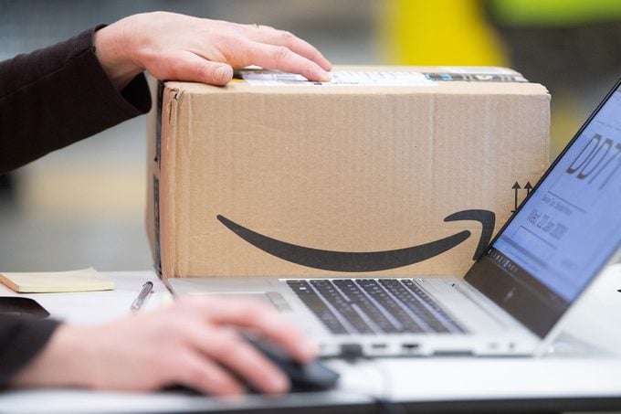 An Amazon sorting employee is working on a laptop in a distribution centre next to a package