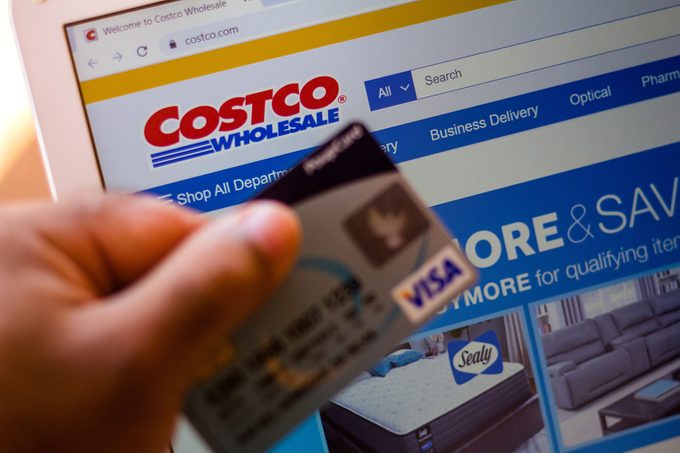 The Costco Wholesale Corporation Website Is Displayed On A Laptop Computer Screen with a person holding a visa card in front of it 