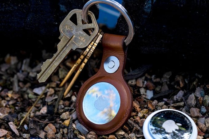 Apple Airtag Hangs on a key ring with house keys on a keyring with a second apple airtag laying in the gravel beside of it