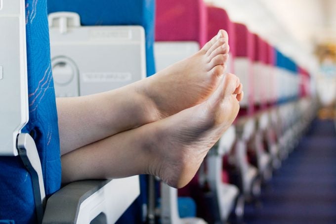 Woman Resting Feet On Seat Armrest Of Commercial Airplane