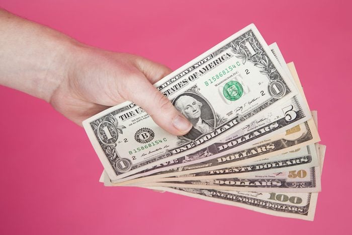 Woman's Hand Holding Assorted US Money Bills on a Pink Background