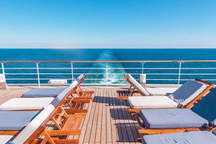 Cruise Ship Deck with chairs looks over the bright blue ocean and the back of the cruise ship