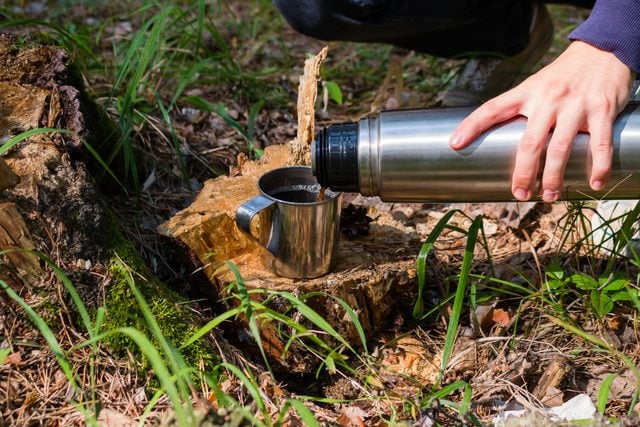hiker pours tea from a thermos in a summer forest