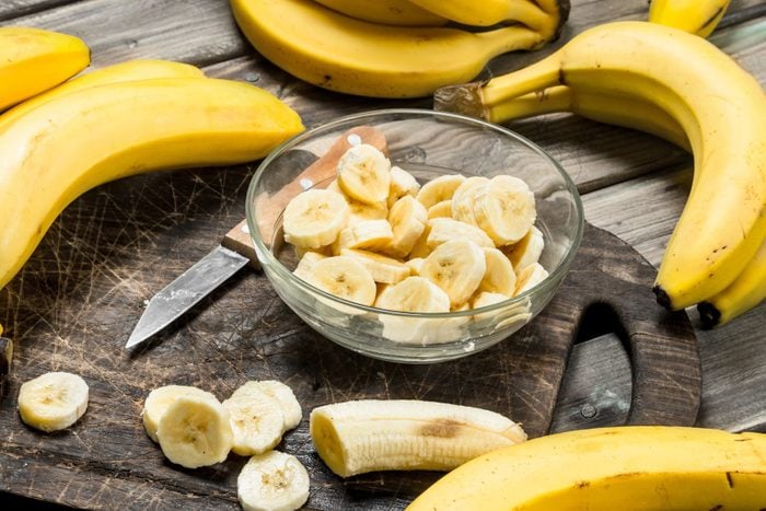 Bananas and banana slices in a plate on a black chopping Board with a knife.