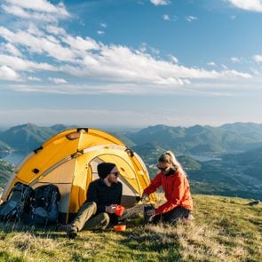 Couple camping on mountain top, prepare food and beverages next to tent