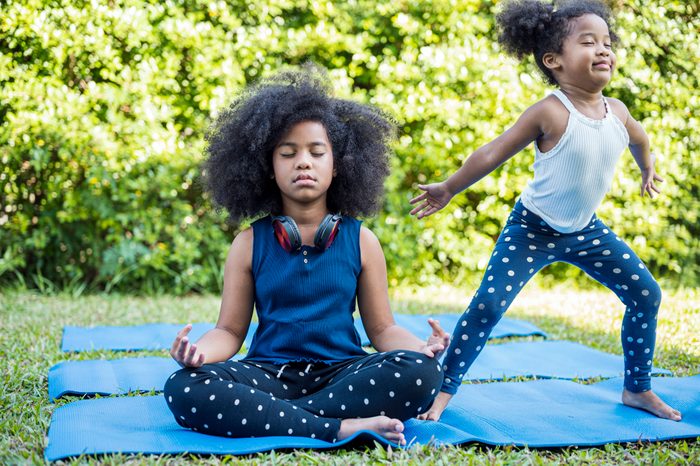 Two little cute girl practicing yoga pose on a yoga mat together at front yard.