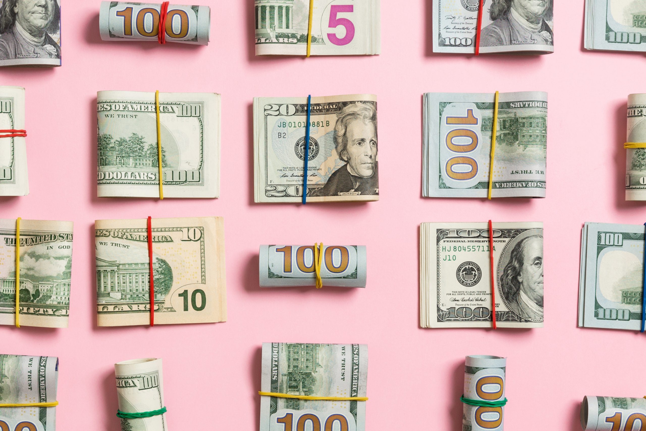 wads and rolls of money arranged on a pink background