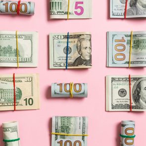 wads and rolls of money arranged on a pink background