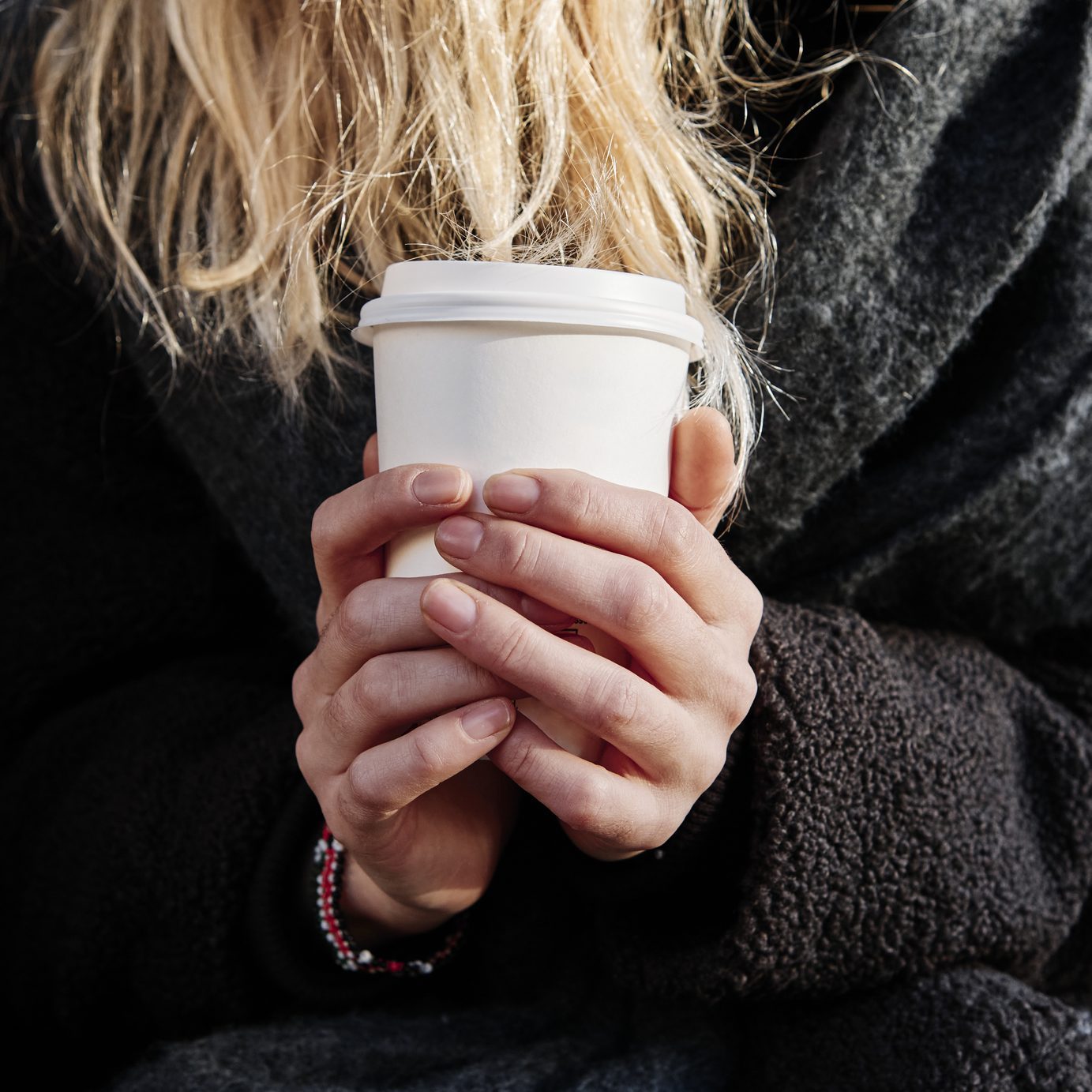 close up shot of blonde female holding a paper cup of coffee with both hands