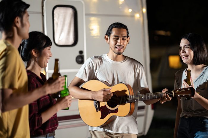 Group of Asian man and woman are having new year party outdoor in the night together. Friends are drinking bottle of beer and drinking with happiness and smile. Travel nature, camping on camper van.