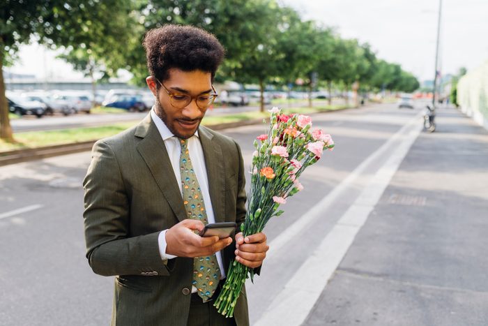 Businessman with bouquet using mobile phone while standing on street