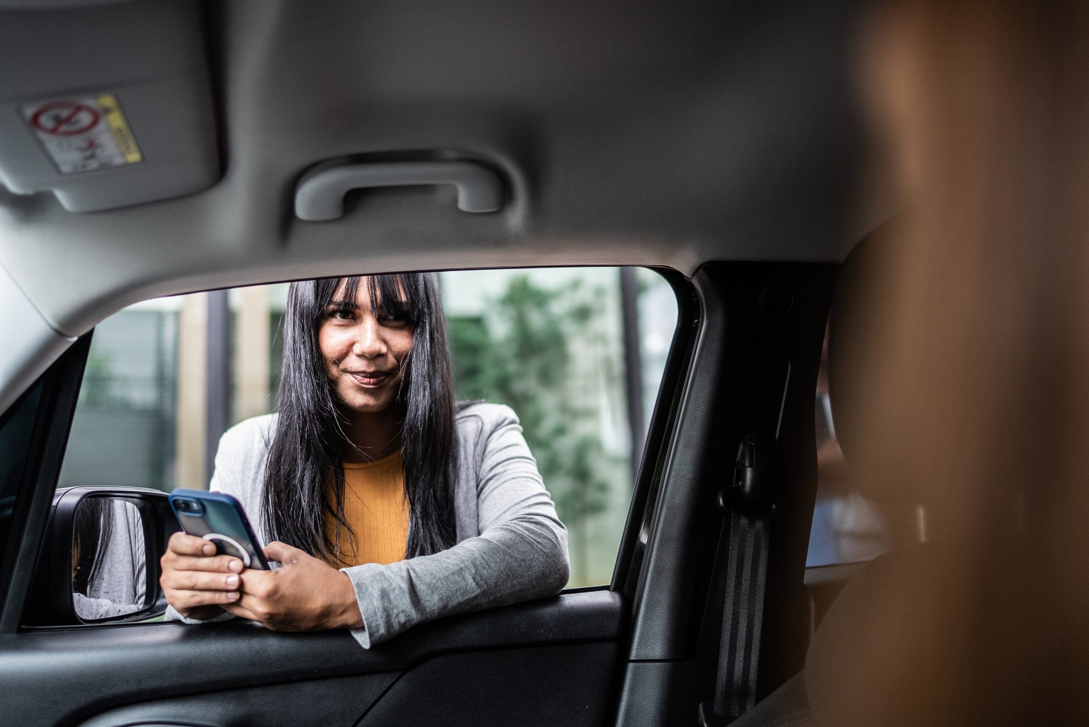 Transgender businesswoman using smartphone talking to cab driver through the car window