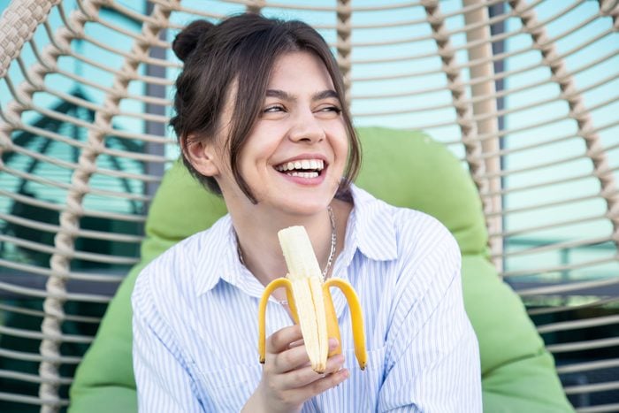 Happy young woman eating a banana while sitting in a hammock.