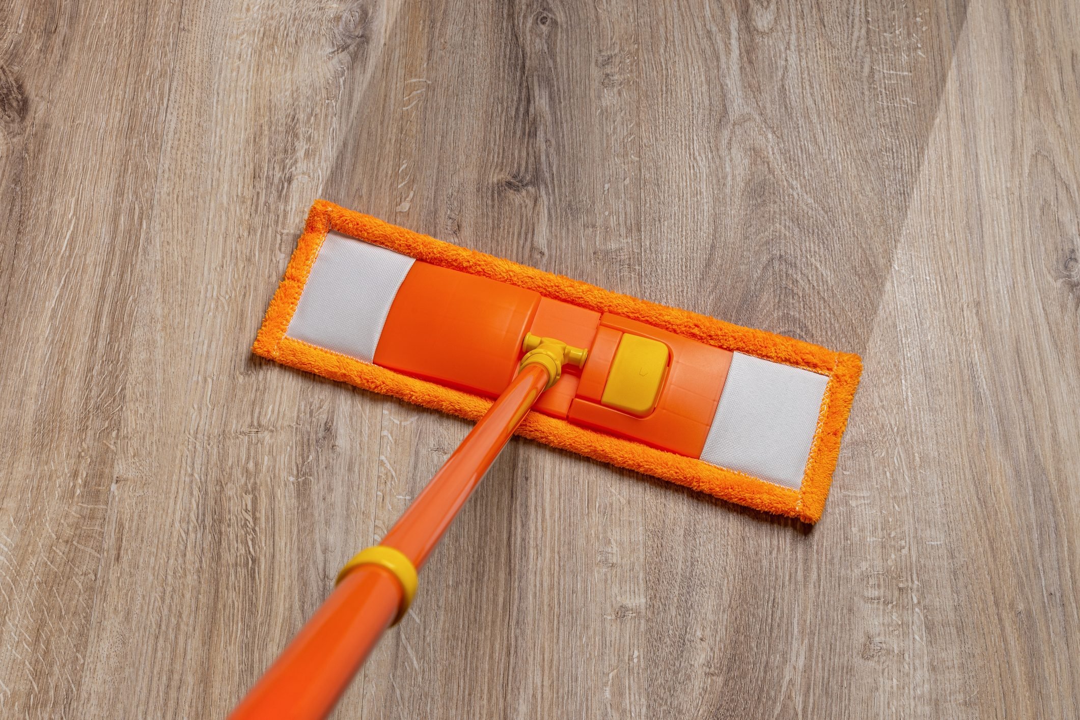 Orange mop washing dusty floor at home. Cleaning the wooden laminate floor with wet microfiber mop. Mopping the floor. Housekeeping, homework routine, cleaning concept.