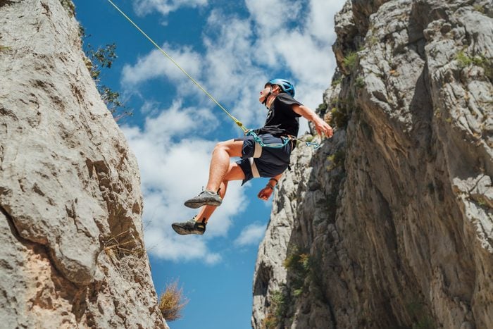 Climber teenager boy in protective helmet abseiling from vertical cliff rock wall using rope Belay device, climbing harness in Paklenica canyon in Croatia. Active extreme sports time spending concept