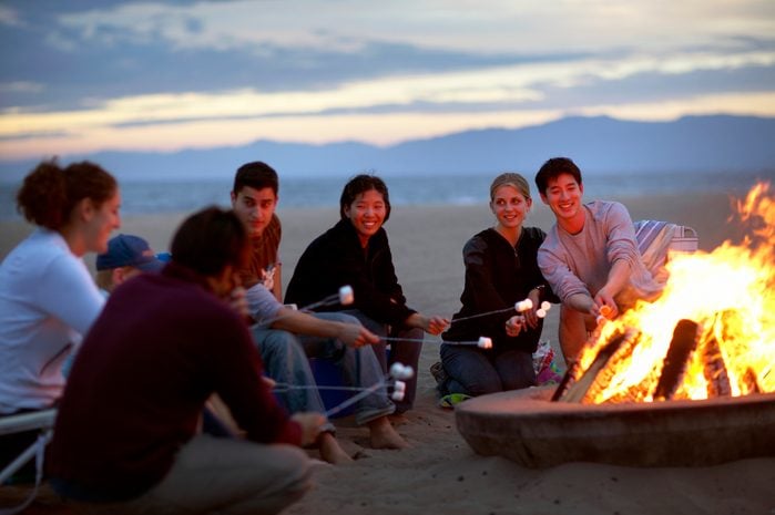 Group of people on beach roasting marshmallows over bonfire
