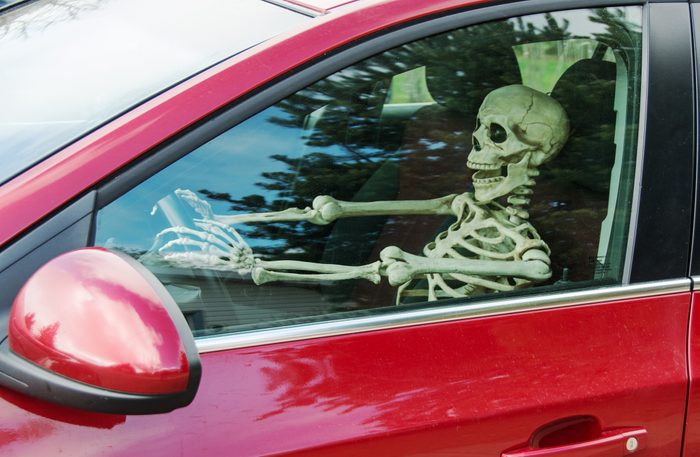 Skeleton driving a car as seen through side window