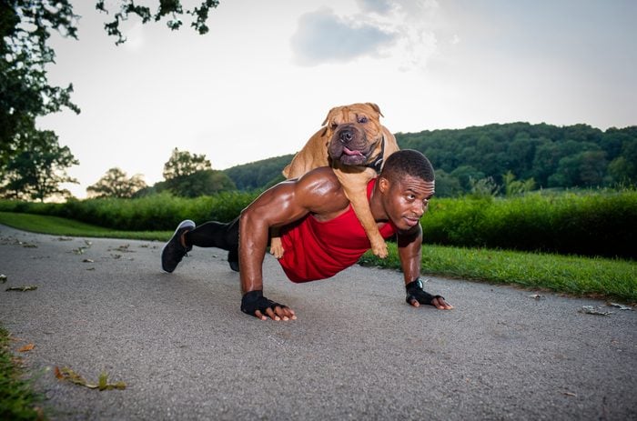 Young man doing pushups on rural road whilst giving dog a piggyback