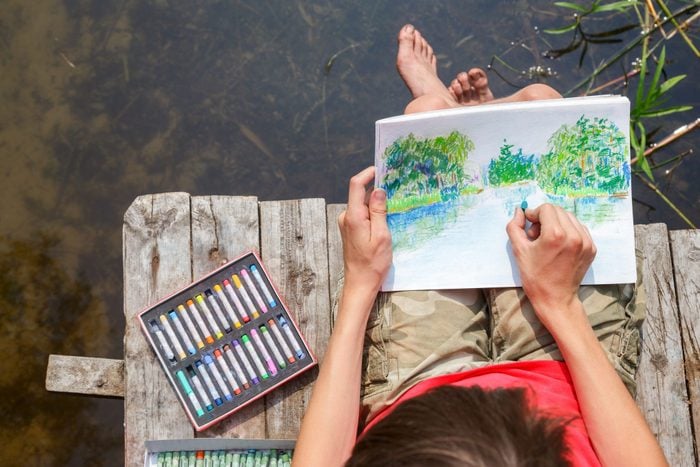 Kid drawing a summer landscape with a forest lake