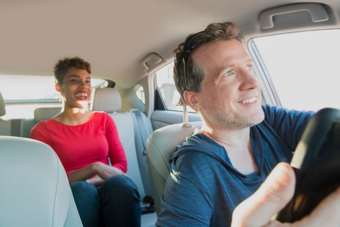 Smiling Male Driver Gives Ride to Smiling Passenger in Backseat