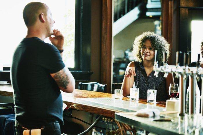 Smiling woman in discussion with bartender while seated at bar
