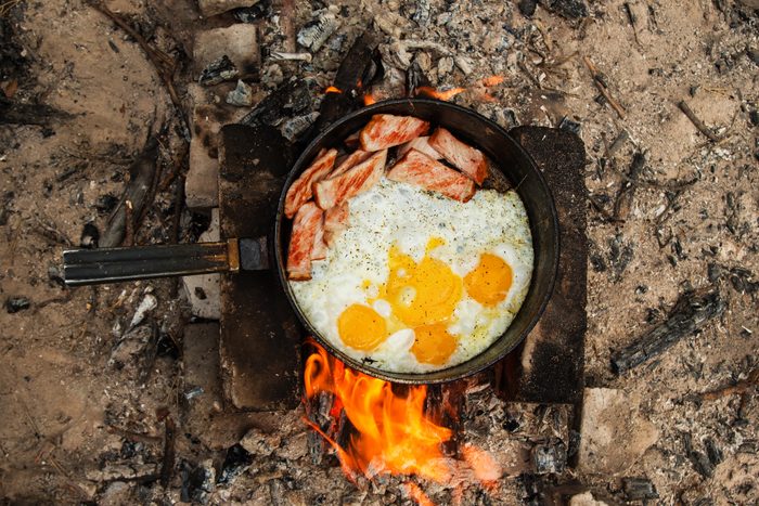 Scrambled eggs with bacon on the cast-iron pan on a bonfire, top view.