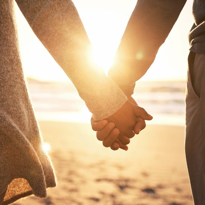 couple holding hands on a beach with the sun shinning