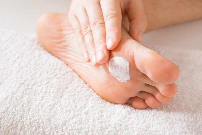 Groomed Young Mans Hand Applying Feet Moisturizing Cream Barefoot On The White Towel Cares About Clean And Soft Legs Skin Healthcare Concept