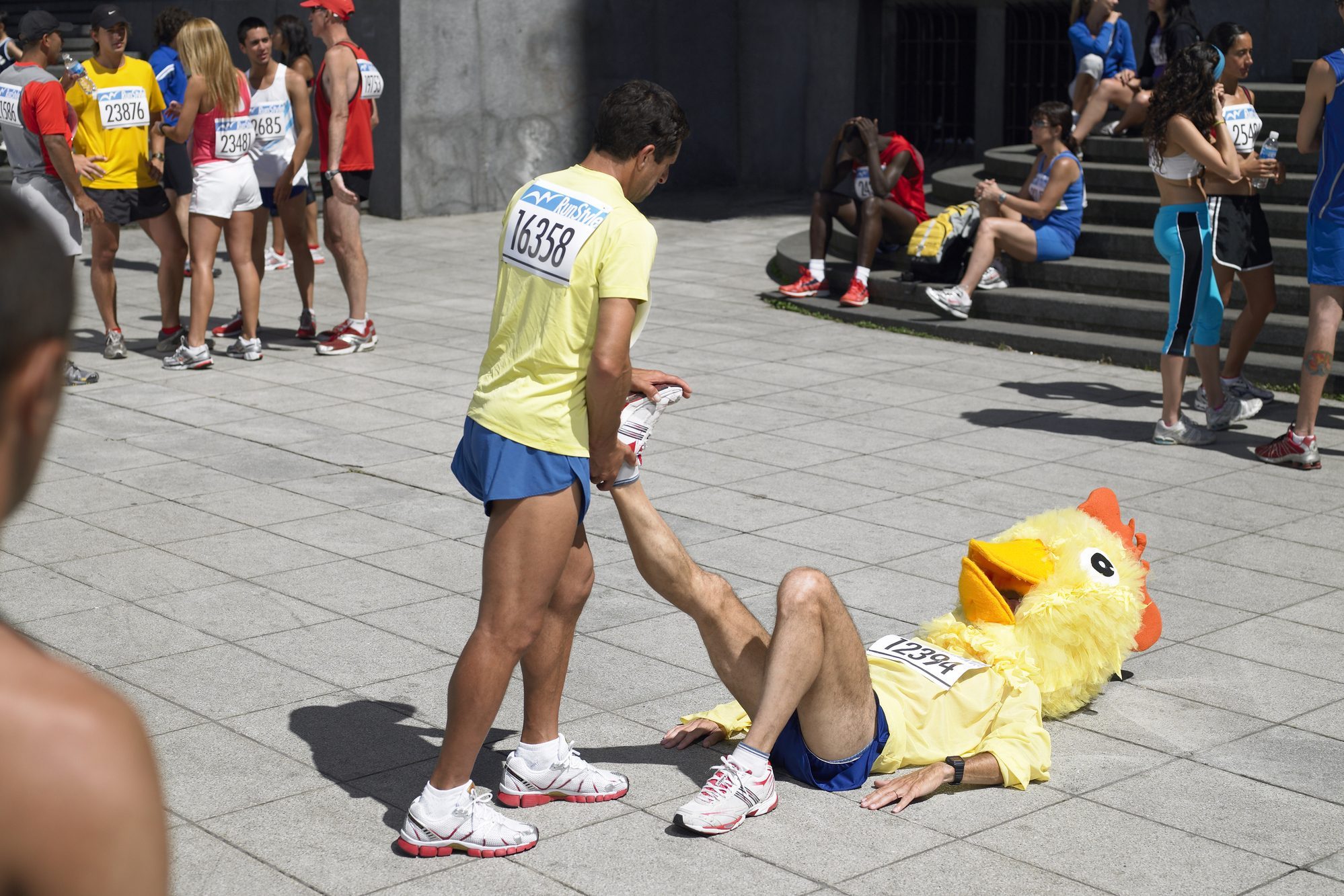 Group of marathon runners stretching on sidewalk, one wearing chicken head