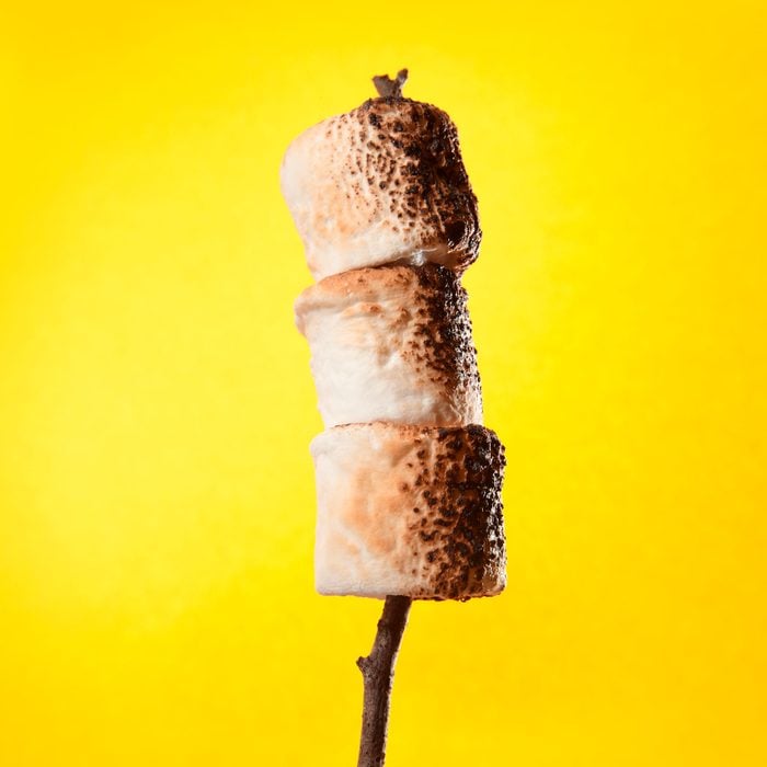 three Roasted Marshmallows On A Stick against yellow background