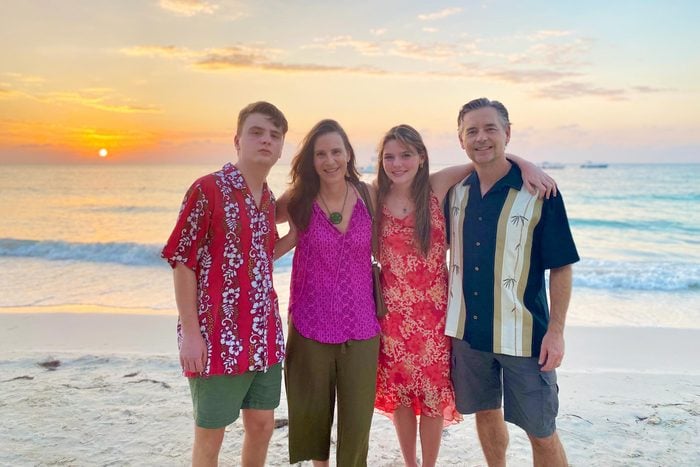 son, mother, daughter and father standing in front of a sunset by the ocean