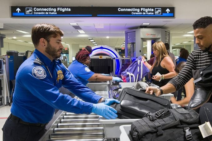 Transportation Security Administration (TSA) agents help travelers place their bags through the 3-D scanner at the Miami International Airport
