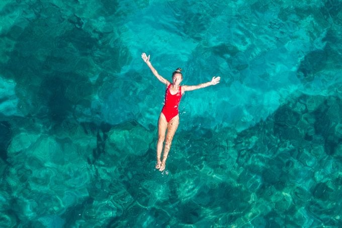 Woman Floating in Turquoise Sea while wearing a red swimsuit