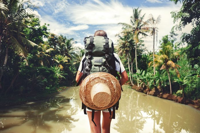Traveler woman with backpack standing near big tropical river on sunny day