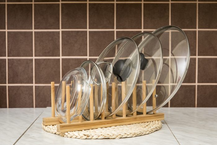 Wooden natural color rack for holding pot/pan lids in kitchen, brown tiles on the background. Kitchen organizer interior element tool concept.