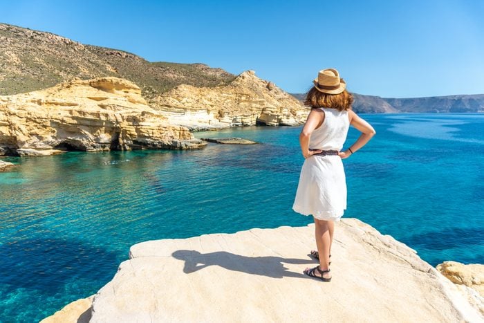 A young woman in a white dress looking at the sea in Rodalquilar in Cabo de Gata on a beautiful summer day, Almería. Mediterranean sea, spain