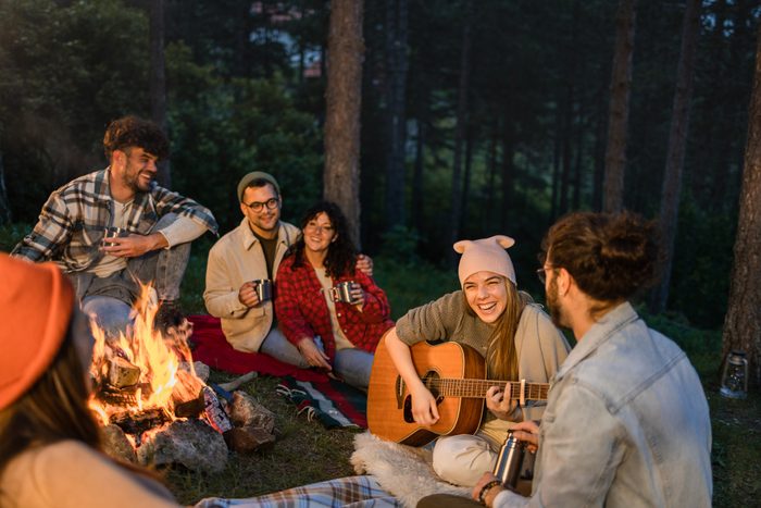 Happy woman playing a guitar to her friends on camping by the bonfire