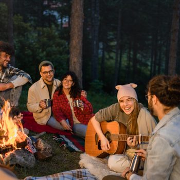 Happy woman playing a guitar to her friends on camping by the bonfire