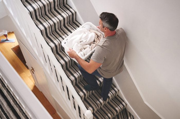 Shot of a man carrying a basket of freshly laundered clothing up stairs