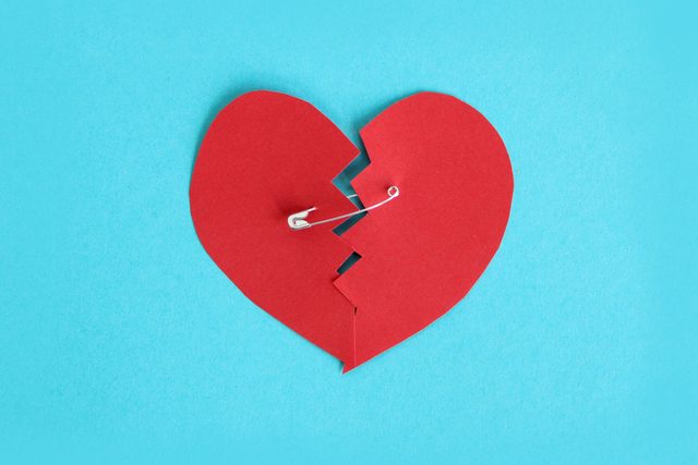 A Broken Heart Sewn With Safety Pin Over Turquoise Background