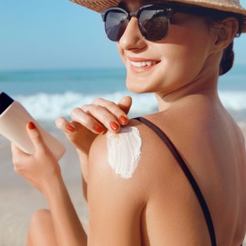 Girl Using Sunscreen to Skin. Beautiful Woman in Bikini Applying Sun Cream on Tanned Shoulder. Sun Protection. Skin and Body Care.
