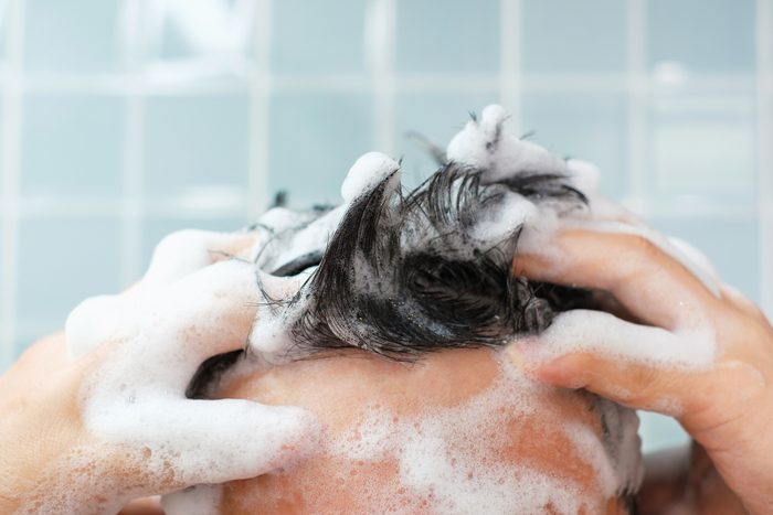 Male hands wash their hair with shampoo and foam on blue background, front view.